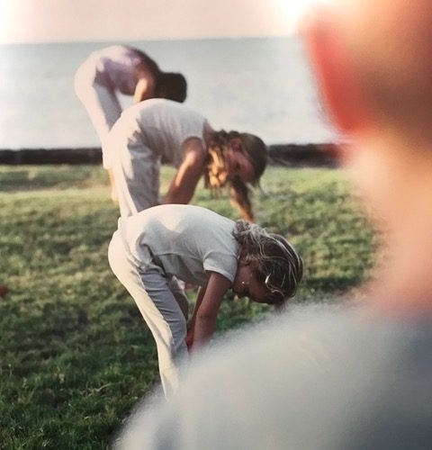 three young girls do forward bend while instructor watches